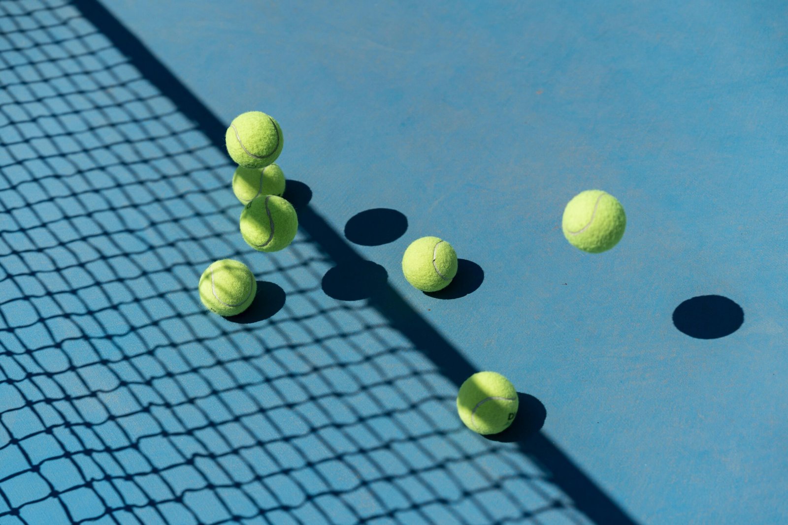 Tennis balls scattered on a blue court casting shadows, captured from above for a high-energy sports vibe.